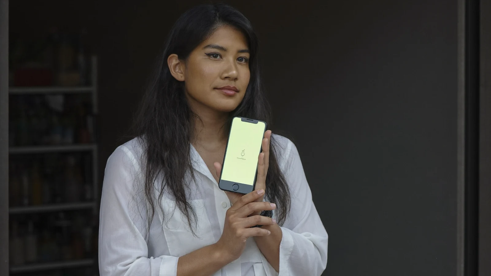 Comerciante na porta da loja segurando o celular com a tela do aplicativo acesa